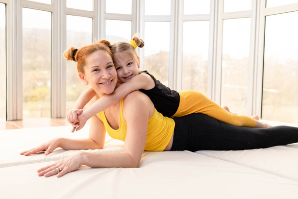 Little girl lying on top of her fit mother in the gym - Foto, imagen