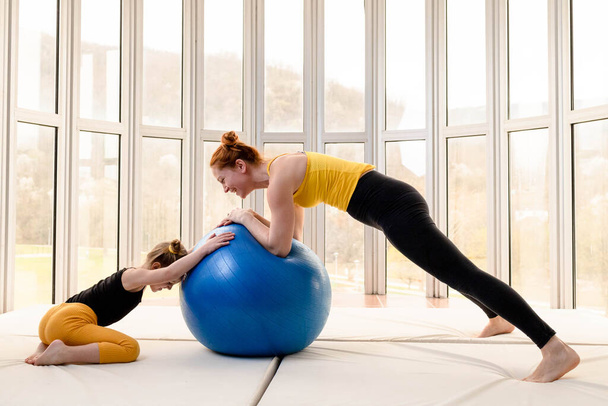 Young fit mom and her daughter having fun with fitness ball in a gym - Fotografie, Obrázek