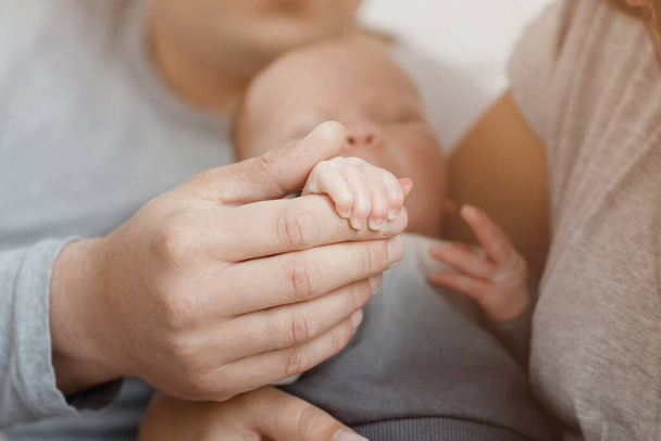 Νέοι γονείς που κρατούν το μικρό χέρι του μωρού. Κοντινό πλάνο των χεριών της μαμάς, του μπαμπά και του μωρού. Παιδική μέριμνα, οικογένεια. - Φωτογραφία, εικόνα
