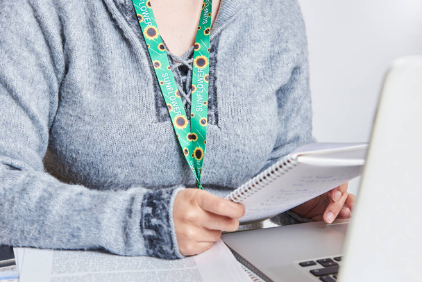 Unrecognizable person studying or working at home using a sunflower lanyard, symbol of people with invisible or hidden disabilities. - Photo, Image