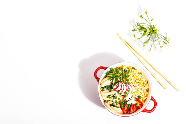 Los fideos asiáticos con pollo, verduras y hierbas están aislados sobre un fondo blanco. Sopa tradicional japonesa con caldo, y flores de cerezo, vista superior - Foto, imagen