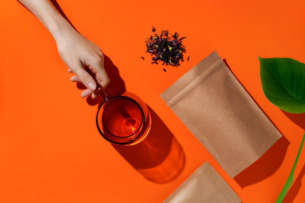 Упаковка коричневого картону для чаю та жіночої руки з чашкою чаю. Макет брендингу та упаковки чаю на помаранчевому фоні. Високоякісна фотографія
 - Фото, зображення