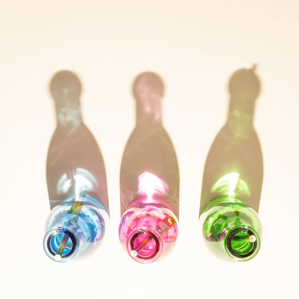 Colorful bottles with cold drinks on sandy background. Shadows with shiny colorized reflections. Aesthetic abstract design idea. Sunny beach day concept. - Photo, image