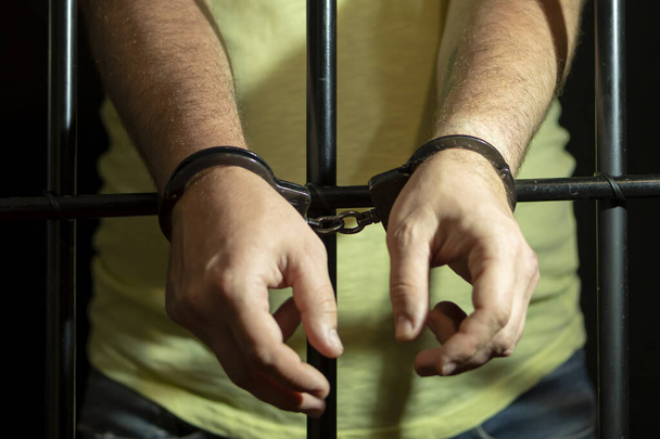 Ein Mann in Handschellen in einer Zelle hinter Gittern. Konzept: ein Gefangener im Gerichtssaal, eine Verurteilung zu einer verurteilten Person, eine Gefängnisstrafe. - Foto, Bild