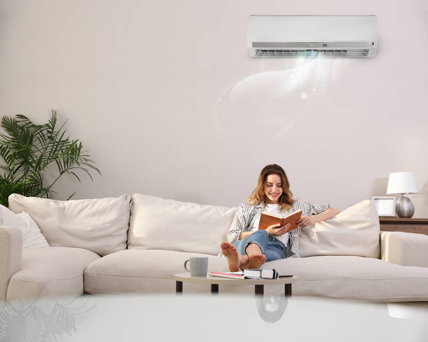 Young woman resting under air conditioner on white wall at home - Photo, Image