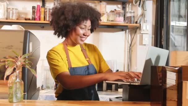 Афро-американская женщина-бариста кафе в случайном фартуке довольна онлайн заказ клиента в ноутбуке, веселая работа с улыбкой в стойке бара в кафе, малый бизнес стартап предпринимательский образ жизни. - Кадры, видео