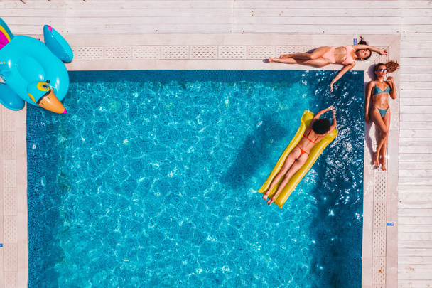 Yüzme havuzunda güneşlenip güneşlenen mayo giymiş arkadaşlar. - Fotoğraf, Görsel
