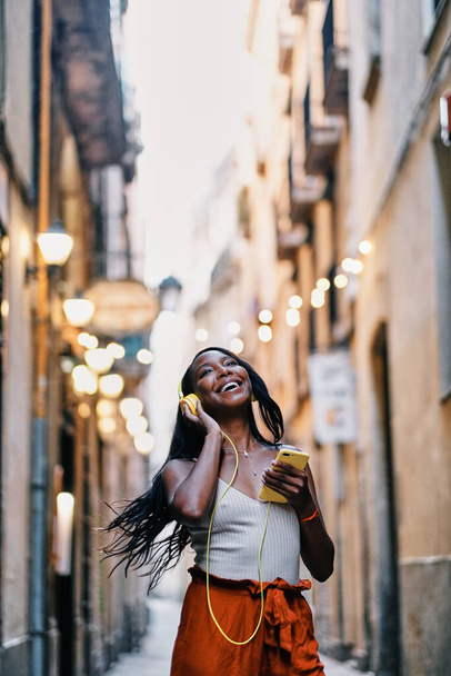 Молода щаслива жінка насолоджується прослуховуванням музики з мобільним телефоном та навушниками на відкритому повітрі
. - Фото, зображення