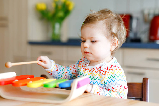 Домашняя симпатичная маленькая девочка, играющая с развивающей деревянной музыкальной игрушкой. Счастливый взволнованный ребенок малыша научиться играть красочные радуги ксилофона. Раннее образование, деятельность для детей. - Фото, изображение