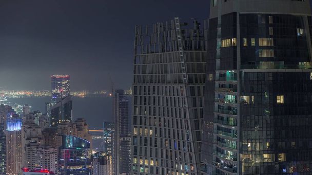 Aerial view of JBR and Dubai Marina skyscrapers and luxury buildings night timelapse from above. Illuminated towers with glowing windows - Фото, изображение