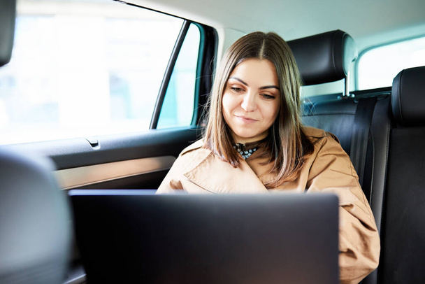 Belle femme d'affaires travaillant sur son ordinateur portable à l'arrière assis d'une voiture sur le chemin de la réunion - Photo, image