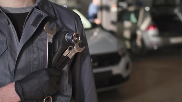 servizio auto, giovane un uomo in uniforme sta in piedi con chiavi regolabili in mano in una stazione di servizio, primo piano - Filmati, video