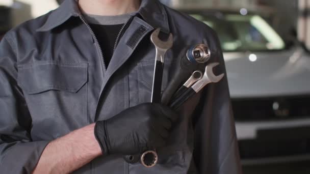 meccanico professionista maschio auto con una chiave regolabile nelle sue mani sta sfondo di una macchina in un centro di servizio, primo piano - Filmati, video