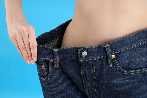 Concept of weight loss, thin girl in jeans on blue background - Photo, Image