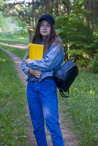 Young female student with blue eyes, folder and backpack on nature background. - Photo, Image