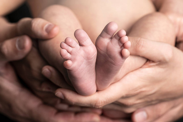 Close up of a baby feet and the hands of his fathers - Foto, afbeelding