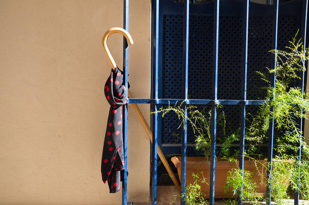 Detail aus dem Gehstock eines Zigeunerpatriarchen auf einem blauen Fenstergitter und einem schwarzen Taschentuch mit roten Tupfen am Stock. Konzept Zigeunerdorf. - Foto, Bild