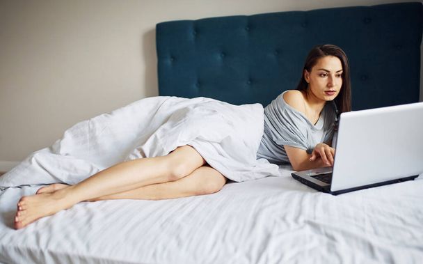 Using laptop. Young woman resting and spending weekend at home alone at home. - 写真・画像