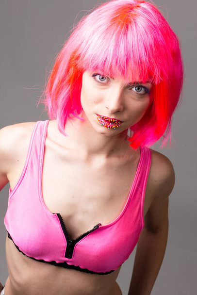 Imagen de la hermosa mujer excitada en la peluca riendo mientras posando con dulces aislados sobre fondo rosa
 - Foto, imagen