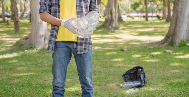 ゴミ収集人の手でペットボトルを拾いゴミを黒いゴミ袋に入れて公園できれいにし汚染を避け環境や生態系に優しい. - 写真・画像