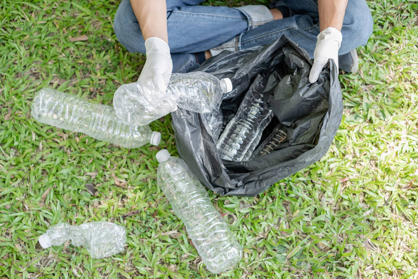 Le mani dell'uomo raccolgono bottiglie di plastica, mettono spazzatura in sacchi neri per pulire nei parchi, evitare l'inquinamento, essere amichevole per l'ambiente e l'ecosistema. - Foto, immagini