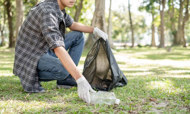 Man's hands pick up plastic bottles, put garbage in black garbage bags to clean up at parks, avoid pollution, be friendly to the environment and ecosystem. - Фото, изображение