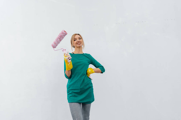 A young girl is engaged in repairs and smiles with a pink roller in her hands against a white wall in a new apartment. Renovation of the interior and a new apartment. Housewarming and a desirable mortgage. - Foto, Imagem