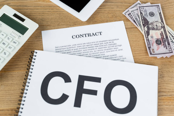 Draufsicht auf Papiere mit CFO und Vertragsaufdruck in Dollarnähe, digitales Tablet und Taschenrechner auf dem Schreibtisch - Foto, Bild