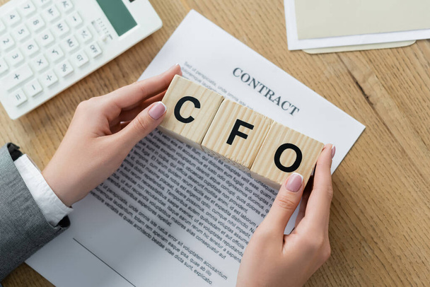 top view businesswoman holding wooden cubes with cfo lettering near contract and calculator  - Photo, Image