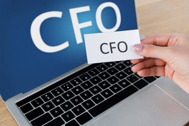 cropped view of woman holding paper near laptop with cfo lettering on screen - Foto, Bild