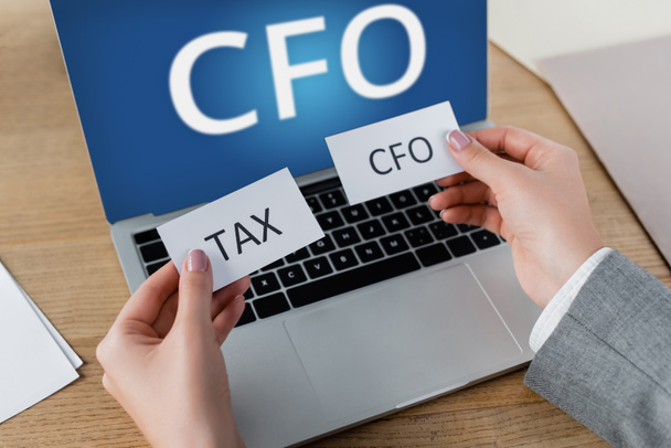 cropped view of woman holding papers with lettering near laptop with cfo on screen - Фото, зображення