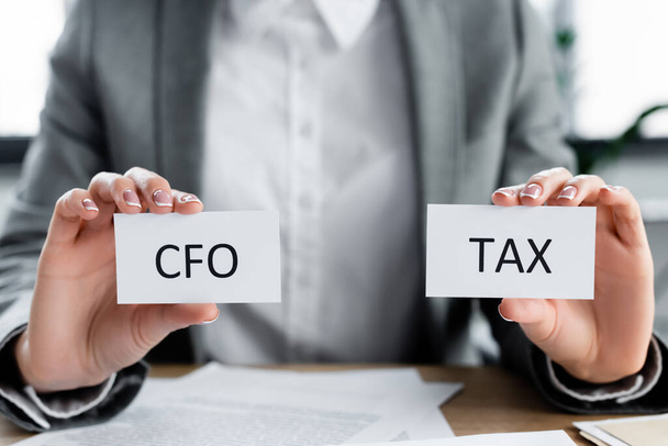 Ausgeschnittene Ansicht einer Frau mit Papieren mit CFO und Steueraufdruck im Büro - Foto, Bild