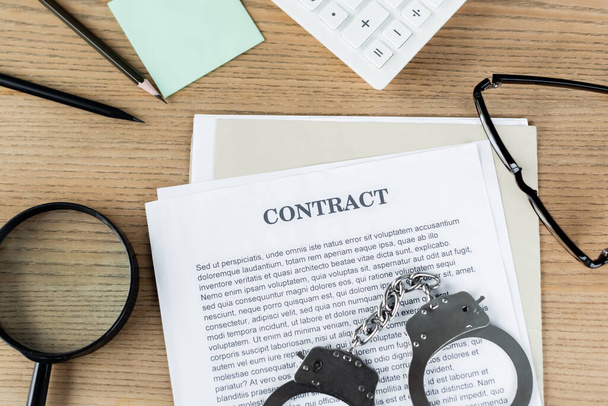 top view of handcuffs on contract near magnifier, glasses and stationery  - Photo, Image