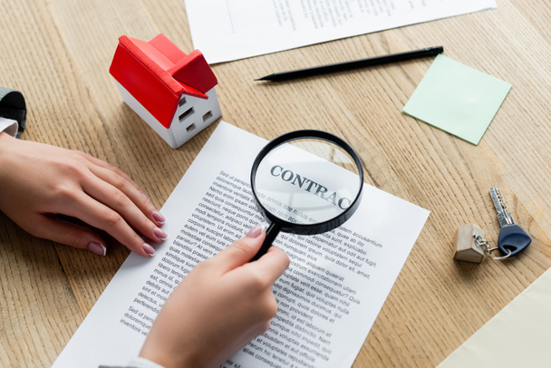 cropped view of tax inspector holding magnifier above contract and house model on desk - Foto, Imagem