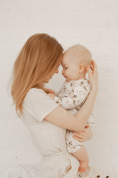 Портрет молодой счастливой мамы, держащей маленького пухлого младенца, трогающего головами на белом фоне. - Фото, изображение