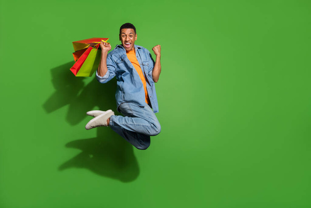 Full length photo of funny man addicted to shopping jumping up in excitement isolated on green color background - Photo, Image