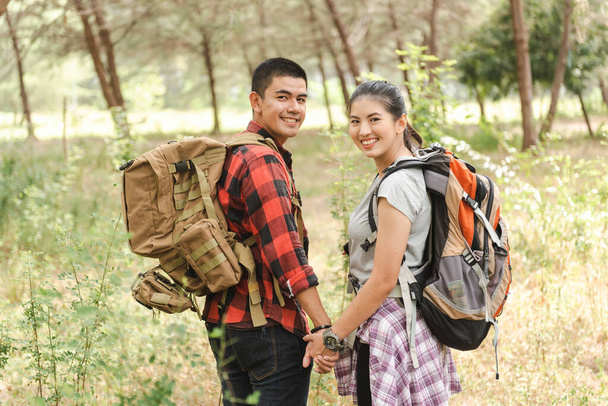 Ασιατικό ζευγάρι πεζοπορία backpacker κρατώντας τα χέρια κοιτάζοντας κάμερα στο δάσος. - Φωτογραφία, εικόνα