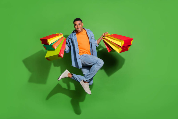 Full length photo of good mood jumping man visit many shops in city center mall isolated on green color background - Zdjęcie, obraz