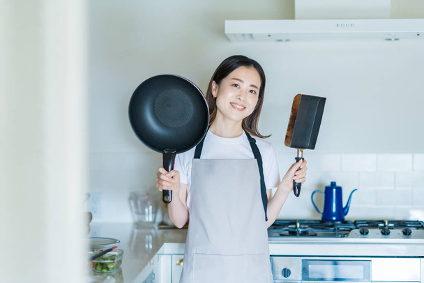 Nainen, jolla on paistinpannu molemmissa käsissä keittiössä - Valokuva, kuva