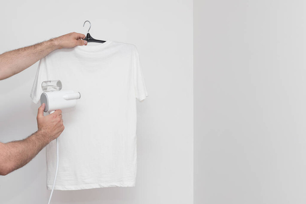 Steam the T-shirt with a portable steamer on a white background. copyspace - Zdjęcie, obraz
