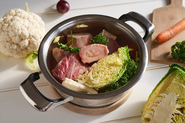Fresh marrow bones, beef meat and vegetables in a pot of water - preparation of homemade broth - Foto, afbeelding