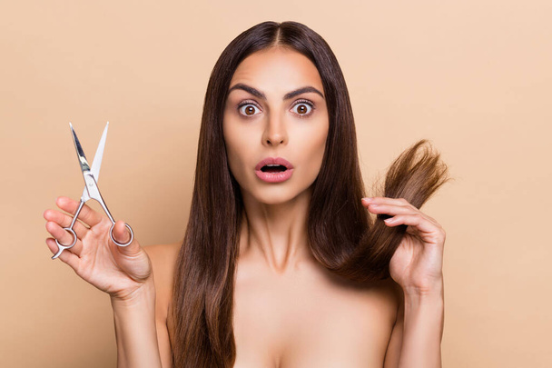 Portrait of attractive worried healthy long-haired girl holding scissors dry ends isolated over beige pastel color background - Фото, зображення