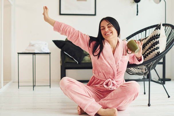 Jovencita alegre en pijama sentada en el suelo en el interior durante el día. - Foto, Imagen