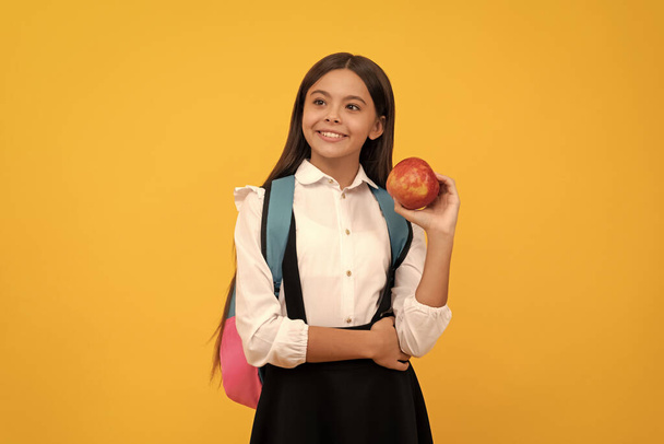Fille heureuse enfant tenir pomme et sac d'école fond jaune, connaissance - Photo, image