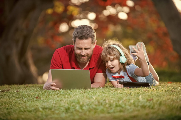 ευτυχισμένη οικογένεια του πατέρα και του γιου χρήση φορητού υπολογιστή και ακουστικά στο πάρκο, ευτυχισμένη οικογένεια. - Φωτογραφία, εικόνα