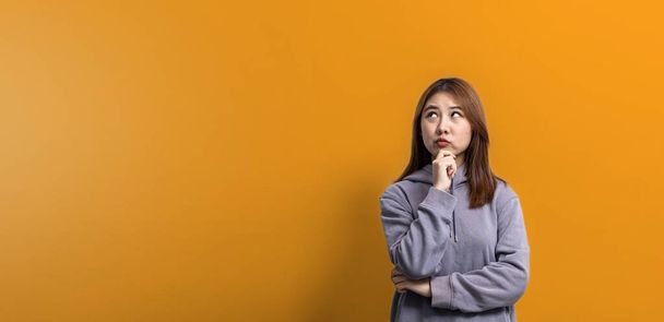 Portrait of beautiful Asian woman expressing thoughtful and doubtful expressions on isolated background, portrait concept used for advertisement and signage, isolated over yellow background, copy space. - Фото, зображення