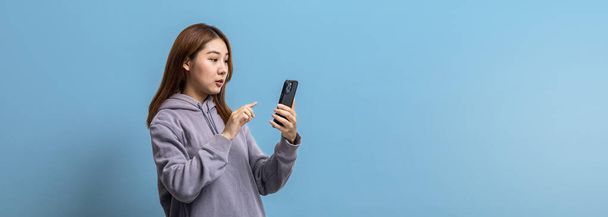 Portrait of beautiful Asian woman holding mobile phone on isolated background, portrait concept used for advertisement and signage, isolated over blue background, copy space. - Φωτογραφία, εικόνα