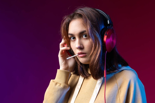 Young beautiful fashionable hipster girl dressed in a hoodie  listening to music in red headphones in a studio red dramatic background - Foto, Imagem
