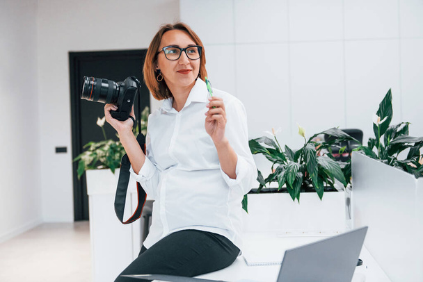 Woman in formal clothes and with camera sitting in the office. - Foto, Bild
