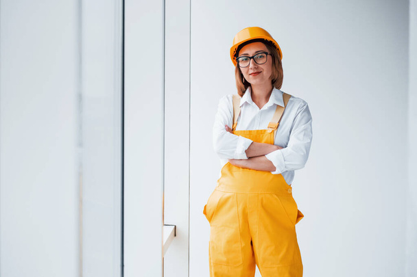 Female worker or engineer in yellow uniform and hard hat standing indoors. - Zdjęcie, obraz